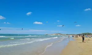 Spiaggia di Scialmarino con kitesurfer che danzano nel cielo azzurro e bagnanti che passeggiano sulla sabbia dorata.