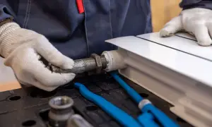 Hydraulik w białych rękawiczkach dokręca metalową rurę do białego grzejnika.