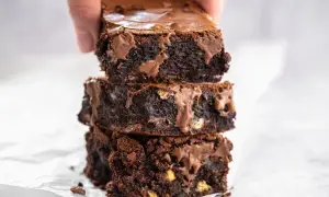 En hand lyfter en stapel saftiga, mörka glutenfria brownies med smält choklad.
