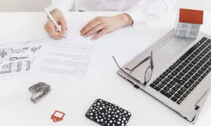 Ręce podpisują dokumenty, obok laptop, model domu i plan. To pokazuje, co oznacza służebność w akcie notarialnym.