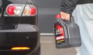 Osoba trzyma olej Motul 6100 Synergie+ SAE 10W40 obok tylnej części czarnego samochodu. Idealny wybór, by dobrze dobrać olej.