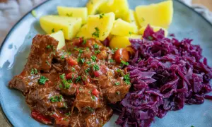 Herzhaftes Gulasch, ein typisches Gericht für schmorgerichte im ofen, serviert mit Salzkartoffeln und Rotkohl.