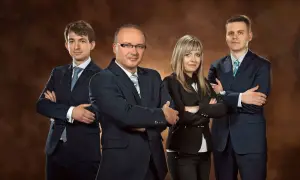 Cztery osoby w garniturach stoją ze skrzyżowanymi rękami na tle brązowym.