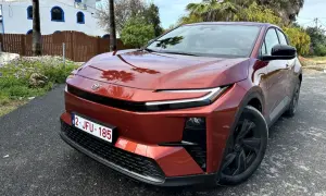Nowa Toyota w kolorze miedzianym, zaparkowana przed białym budynkiem z niebieskimi oknami.
