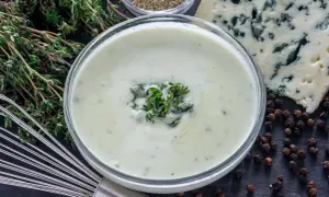 Crema suave y sedosa, lista para tu salsa roquefort receta. Ingredientes frescos como tomillo y pimienta negra completan la escena.