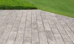 Pavimentazione marciapiede in cemento stampato effetto legno, adiacente a un prato verde ben curato.