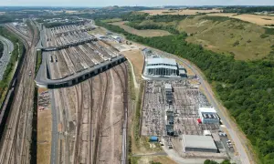 Rozległa infrastruktura kolejowa i stacja transformatorowa przy Eurotunelu. W tle wzgórza z białym koniem.