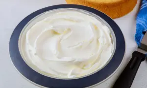 Puszysta bita śmietana z mascarpone w misce, gotowa do dekorowania tortu. Obok leżą biszkopty i szpatułka.