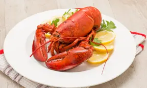 Homard rouge vif, prêt pour la cuisson, servi sur une assiette blanche avec des quartiers de citron et du persil.