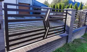 Nowoczesne, najładniejsze ogrodzenia kute z metalu, osadzone na ceglanym murku, tworzą elegancką barierę.