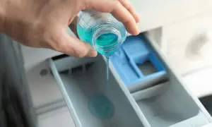 Mano versa liquido blu nel cassetto della lavatrice, mostrando dove mettere il Calgon per un bucato impeccabile.