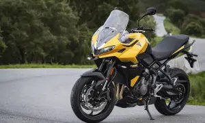 Żółty motocykl uniwersalny Triumph Tiger Sport 660 na krętej drodze wśród zieleni.