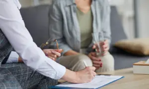 Psychoterapeutka pisze na dokumentach, druga osoba trzyma szklankę wody.