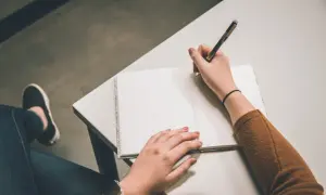 Osoba pisze długopisem w notatniku. Może to być początek pisania listu motywacyjnego po angielsku.