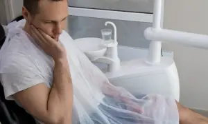 Mężczyzna w fotelu dentystycznym, z ręką na policzku, martwi się o swoje zdrowie. Czy to początek sepsy od zęba?