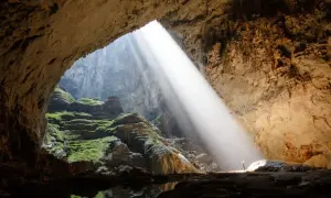 Promień słońca wpada do jaskini Son Doong, oświetlając zielone mchy i skalne tarasy.