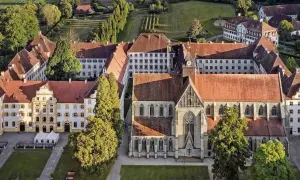 Luftaufnahme eines beeindruckenden schloss im Bodenseekreis mit roten Ziegeldächern, umgeben von grünen Bäumen und gepflegten Gärten.