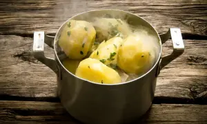 Gorące, gotowane ziemniaki w garnku, posypane natką pietruszki. Idealne, gdy zastanawiasz się, ile gotować ziemniaki, by były miękkie.