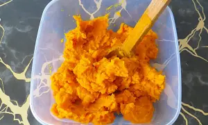 Jasne, oto opis:

Pomarańczowe, gęste puree z dyni hokkaido w plastikowym pojemniku, z drewnianą łyżką.
