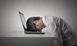 Zrezygnowany mężczyzna z głową na laptopie. Czas na naukę, jak zmienić negatywne myślenie na pozytywne.