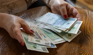 Dłonie z czerwonymi paznokciami trzymają stos polskich banknotów. Pytanie brzmi, ile razy można dać darowiznę dziecku.