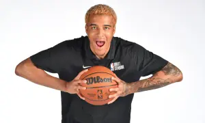 Młody polak w NBA, z blond włosami i tatuażami na ramionach, trzyma piłkę do koszykówki.