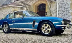 Blå Jensen Interceptor parkerad framför ett stenhus.