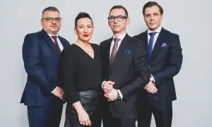 Cztery osoby w garniturach i czarnej bluzce, stojące obok siebie na jasnym tle.