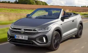 Szary Volkswagen T-Roc Cabrio jedzie po drodze, z otwartym dachem, w słoneczny dzień.