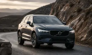 Mörkgrå Volvo XC60 på en slingrig väg i bergig terräng. Solnedgången lyser upp himlen. Kanske en volvo v60 hybrid problem?