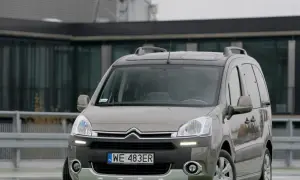 Szary Citroen Berlingo 1.6 HDI z relingami dachowymi zaparkowany przed nowoczesnym budynkiem.