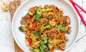 Enkel mat: en skål med nudlar med kyckling, broccoli, paprika och cashewnötter. Röd pinnmat ligger bredvid.