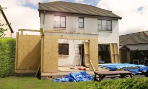 Ein **Anbau Haus** im Bau. Holzkonstruktion und OSB-Platten bilden die Wände des neuen Gebäudeteils. Blaue Planen schützen Baumaterialien.