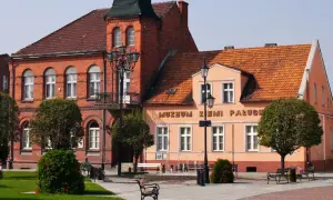 Muzeum Ziemi Pałuckiej, z ceglaną fasadą i pomarańczowym budynkiem, otoczone zielenią i fontanną.