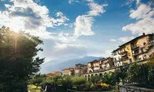 Case colorate si affacciano su un fiume, incorniciate da montagne e cielo azzurro. Un incantevole scorcio dei borghi di Brescia.