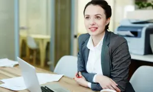 Una consulente HR sorride mentre lavora al suo laptop, analizzando dati e preparando strategie per il personale.