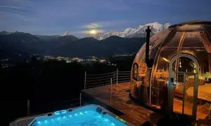 Un jacuzzi illuminé et une bulle transparente, un logement insolite montagne offrant une vue spectaculaire sur les sommets enneigés et la vallée scintillante.