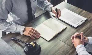 Avvocato e cliente discutono, con un martelletto da giudice e un quaderno aperto. Il ctu significato è fondamentale per la giustizia.