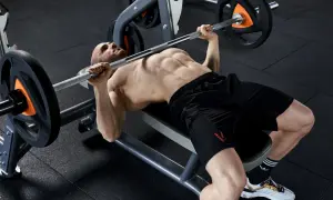 Uomo muscoloso esegue un allenamento powerlifting con bilanciere su panca piana in palestra.