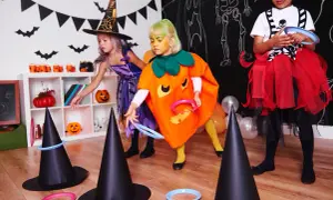 Niñas disfrazadas de bruja y calabaza juegan a lanzar aros en sombreros de bruja, parte de divertidos juegos de Halloween para niños.