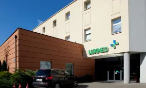 Budynek kliniki Luxmed z zielonym logo, samochód i pomarańczowe pachołki.