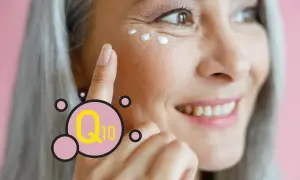Mujer sonríe mientras se aplica crema en el contorno de ojos. El Q10 es un ingrediente clave para el cuidado de la piel.