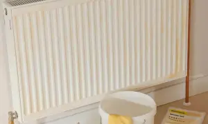 Ein weißer Heizkörper mit gelblichen Flecken, bereit zum heizung streichen. Daneben ein Eimer mit gelben Handschuhen und Malerzubehör.