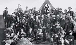 Grupa mężczyzn w mundurach i kapeluszach, z flagą NSDAP w tle. To zdjęcie pokazuje członków partii nazistowskiej, czyli NSDAP.