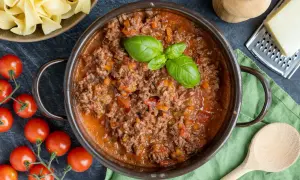Herzhaftes Bolognese-Rezept original: Hackfleischsauce mit Tomaten, Karotten und Basilikum, daneben frische Pasta, Tomaten und Parmesan.