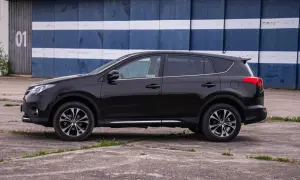 Czarny, używany Toyota RAV4 z salonu, zaparkowany przed budynkiem z niebiesko-białymi pasami.