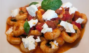 Anellini alla pecorara con pomodoro, zucchine e ricotta fresca, guarniti con foglie di basilico.