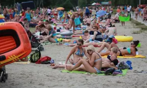 Tłum ludzi odpoczywa na plaży nad jednym z lubelskich jezior. Wszyscy w strojach kąpielowych, opalają się i relaksują.