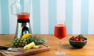 Pyszny koktajl owocowy w kieliszku, obok ananas, truskawki i blender.