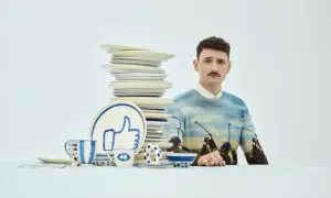 Mężczyzna z wąsikiem w swetrze z motywem polo, obok stosu talerzy i zastawy z symbolem "like". Stylizacja jak z lat dwudziestych.